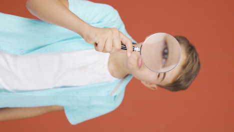 Vertical-video-of-Boy-looking-at-camera-with-magnifying-glass.